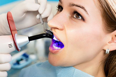 A woman receiving dental care with a device that appears to be a dental laser, while a dental professional attends to her using a handheld device.