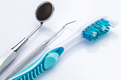 The image displays a collection of dental instruments and tools, including a toothbrush with blue bristles, along with a pair of scissors and other dental implements, all laid out on a white background.