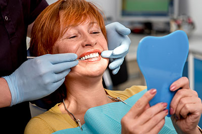 A woman sitting in a dental chair with a smile on her face, receiving dental care from a professional wearing gloves and a mask.