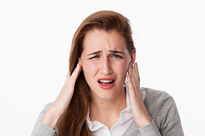 The image shows a woman with her hand on her head, possibly indicating pain or discomfort, with an expression of concern or distress.