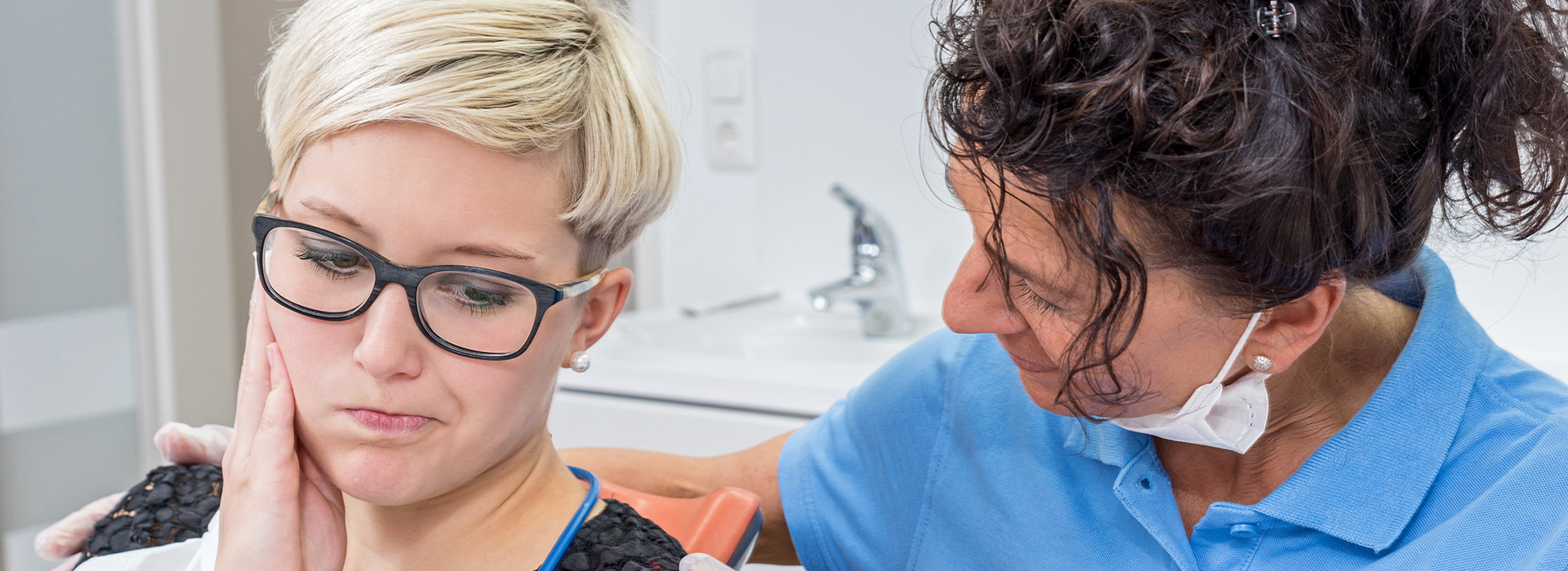 The image shows a woman with short hair receiving dental care from a professional in an office setting.