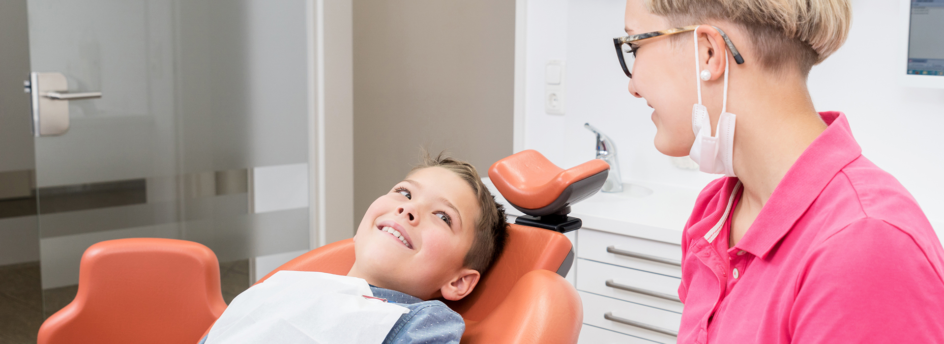 A dental office scene with a dentist assisting a young patient during a dental checkup.