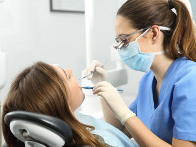 A dental hygienist is performing teeth cleaning on a patient, with both individuals wearing masks and gloves.