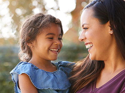 A woman and a child are smiling at each other outdoors.