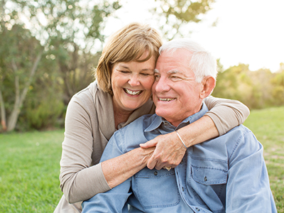 The image shows an elderly man and woman embracing each other outdoors during daylight.