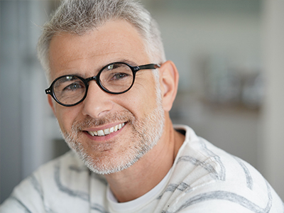 The image shows a man with glasses, wearing a white t-shirt, smiling at the camera.